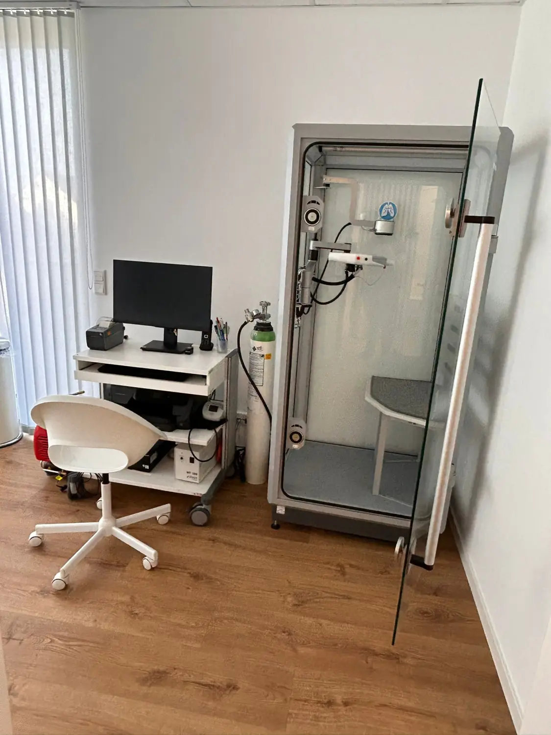 Facharztpraxis für Innere Medizin/Pneumologie – Diagnostik und Therapie - Untersuchungsraum mit HNO-Stuhl, Computer, Sauerstoffflasche und Rollstuhl