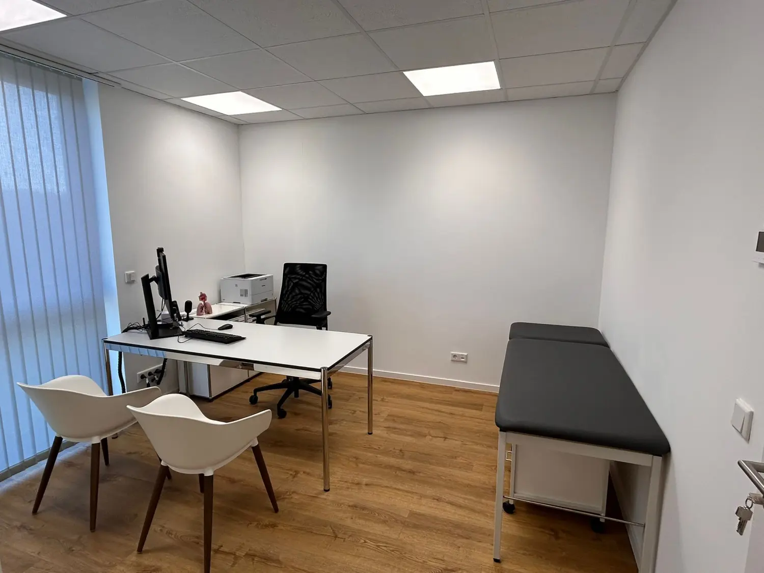 Facharztpraxis für Innere Medizin/Pneumologie – Diagnostik und Therapie - Ein Behandlungsraum mit Computermonitor, Tastatur und Drucker auf dem Schreibtisch und Untersuchungsliege.